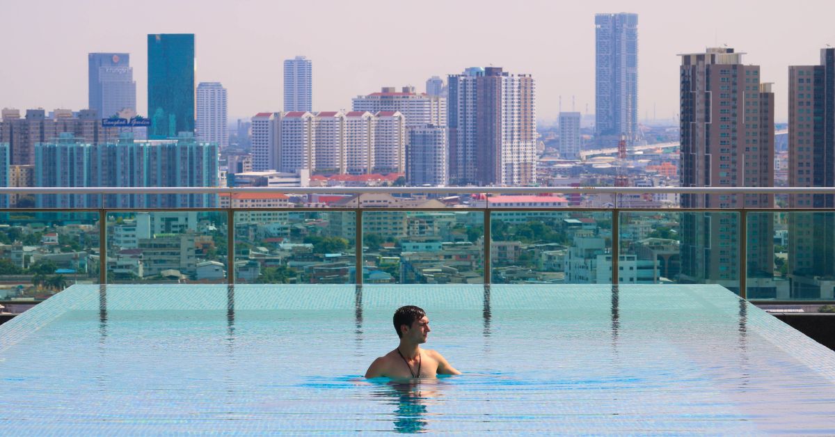 A man is relaxing in the rooftop open-air swimming pool with the view of Bangkok city scape.