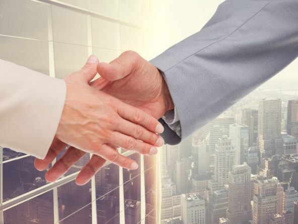 A two business person in white and gray attire is shaking hand with the view of city.