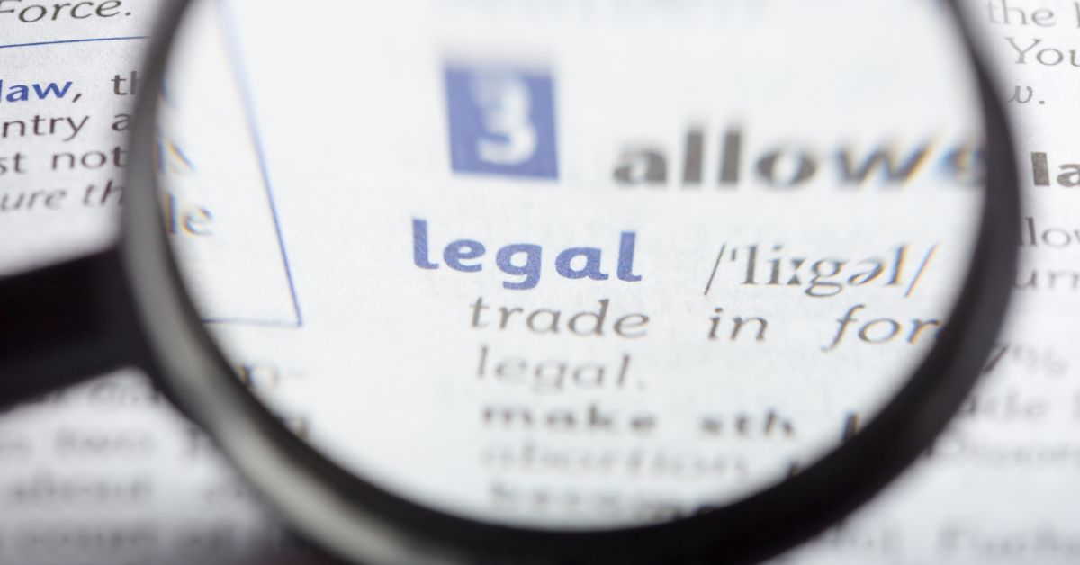 A magnifier is above a dictionary and positioned on a word "legal". 